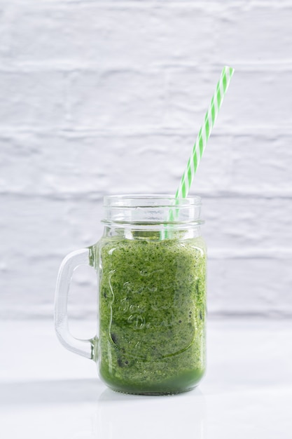 Green detox smoothie in a jar with a straw on white