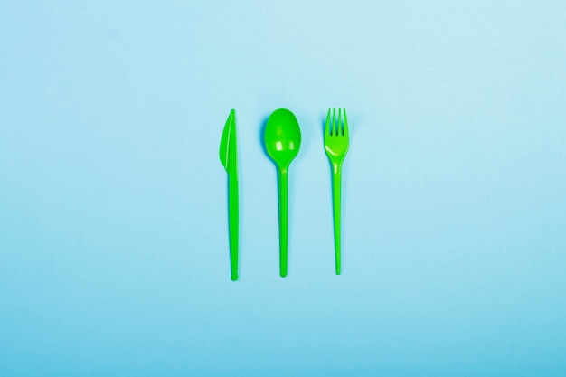 Photo green disposable plastic tableware and appliances for food on a blue background. fork, spoon and knife. concept plastic, harmful, environmental pollution, stop plastic. flat lay, top view.