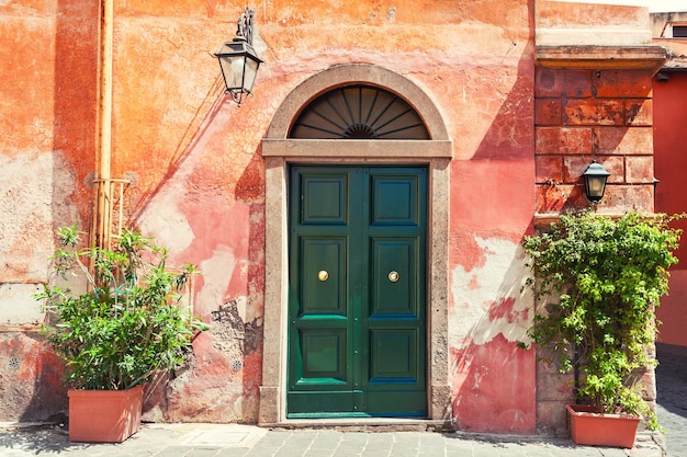 Зеленая дверь на старой красной стене дома. Рим, Италия.