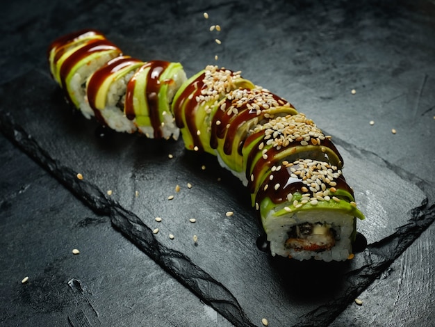 Green dragon avocado sushi rolls on dark background with sesame seeds sprinkled from above. Creative food photography art.