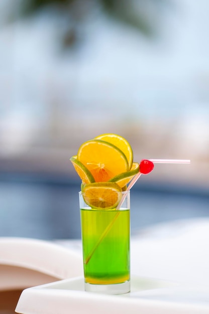 Green drink with orange and cherries by the pool with blurred background