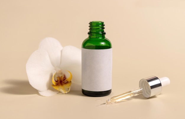 Стеклянная бутылка с зеленой капельницей рядом с белыми цветами орхидеи на светло-желтом продукте Mockup Skincare