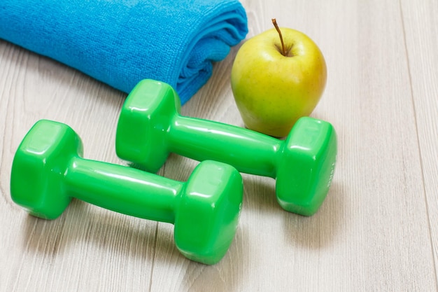 Green dumbbells for fitness an apple and a towel on the background