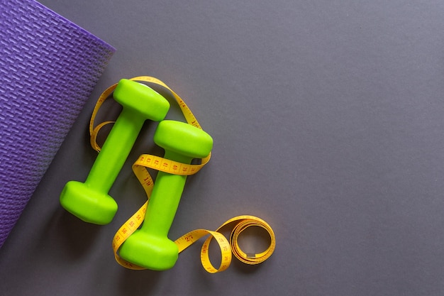 Green dumbbells and a gym Mat on a dark gray paper background . Your text is there. The concept of sports lifestyle.