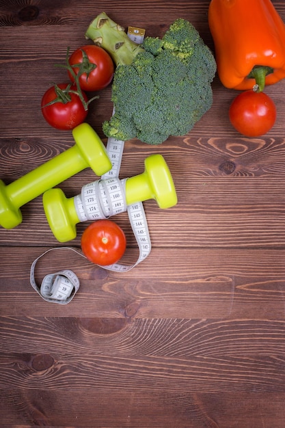Green dumbbells, tomatoes, and tomatoes on a wooden table