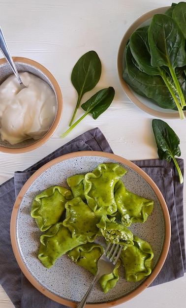 Green dumplings with cottage cheese and spinach on ceramic plate with gray textiles. Vertical, top view.