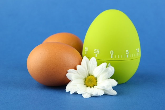 Green egg timer and eggs, on color surface