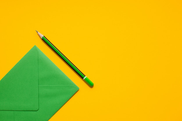 Green envelope and simple green pencil on a yellow background, top view, with copyspace.