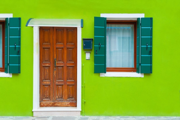 Зеленый фасад дома с деревянной дверью и окнами. Красочная архитектура на острове Бурано, Венеция, Италия.