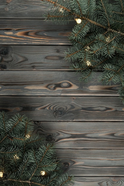 Green fir branches on wooden gray wall flat lay Interior decoration from christmas tree and garland lights Decorative planking for design Dark hardwood material New Year or Christmas holiday