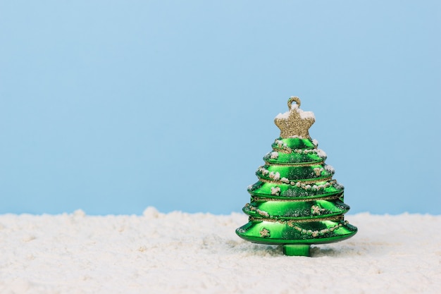 A green fir tree toy with decorations in the snow on a blue background. The concept of meeting Christmas.