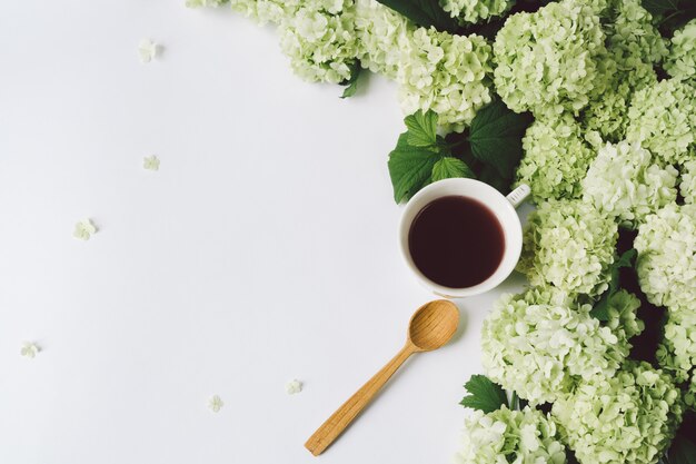 Green flowers, yellow cup with tea and a wooden spoon on a white background