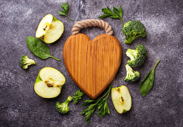 Green food background with wooden board in shape of heart