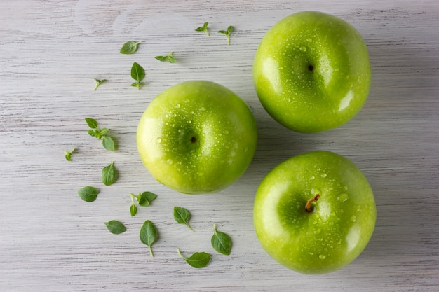 緑の新鮮なリンゴと木製のテーブルにいくつかのバジルの葉