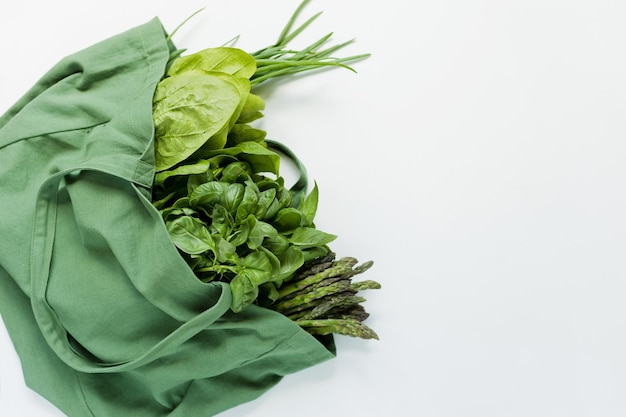 Green fresh herbs in green shopping bag on a white background with copy space Farm market fresh vegetables delivery concept