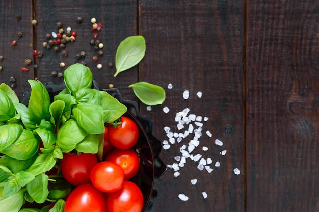 Green fresh leaves of organic basil and small ripe tomatoes and pepper on a wooden table for a healthy diet. Top view. Free space for your project.