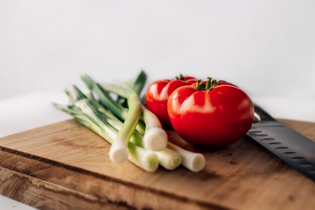 Green fresh onion and tomato on the wooden background. Copyspace.