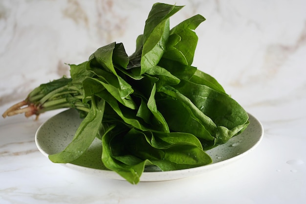 Green fresh spinach leaves lie in a plate on a marble table