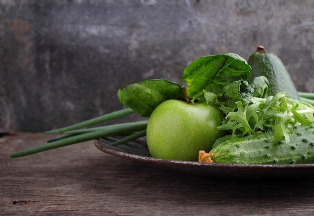 Green fresh vegetables: cucumber, lettuce, onion, avocado, apple on old background