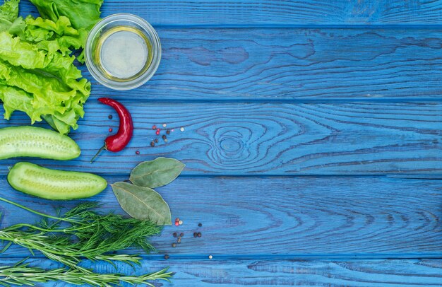 Green fresh vegetables and spices on a blue wooden table. Top view. Place for text