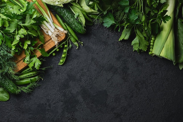 Green fresh vegetables and wooden cutting board on a black textured surface