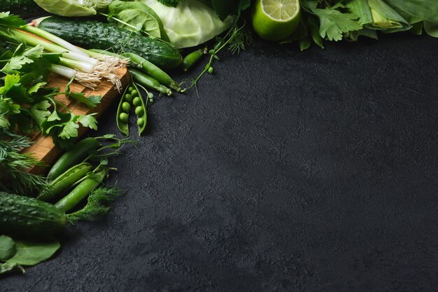 Photo green fresh vegetables and wooden cutting board on a black textured surface