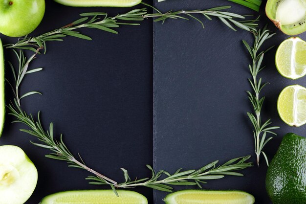 Green fruits vegetables and rosemary on black background avocado kiwi lime and apple on slate board top view copy space