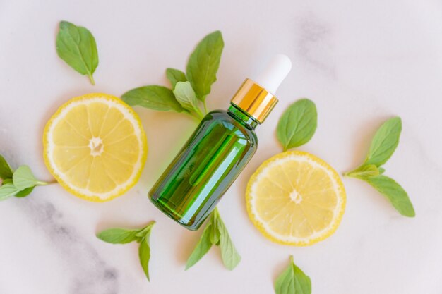 Green glass bottle with a pipette, slices of lemon with mint leaves on a marble background