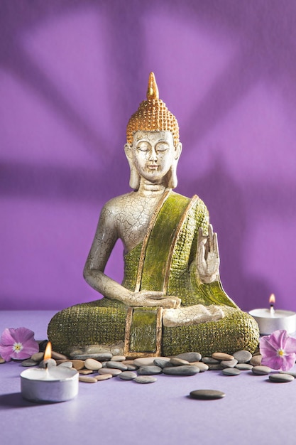 Green and golden buddha statue in meditation with shadows on light purple background Vertical format