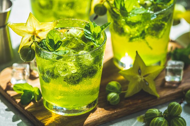 Green gooseberry and carambola cocktail with liqueur ice and fresh mint on a light gray concrete table refreshing summer drink sunny light or detox drink