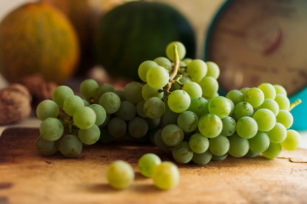 Зеленый виноград лежат на деревянной доске. На заднем плане тыквы, грецкие орехи и весы.
