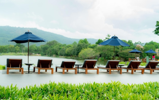 Photo green grass on blur wooden beach chair and beach umbrella beside swimming pool at luxury hotel near