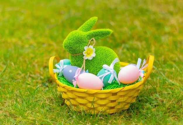 Фото Зеленый травяной кролик в корзине с разноцветными яйцами на лугу, символ пасхи, декор, фигурка кролика