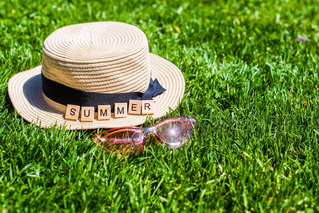 On the green grass a straw hat, sunglasses and wooden letters. word summer. summer background. vacation, weekend.