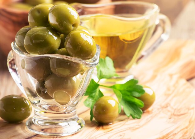 Green greek olives in glass bowl on the vintage wooden background selective focus