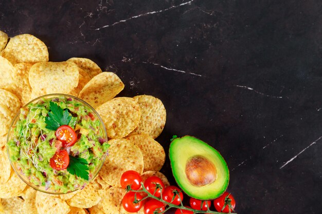 Green Guacamole with nachos and avocado on stone background