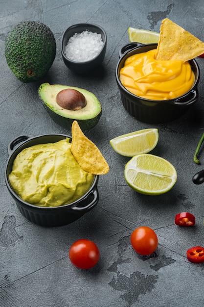 Green guacamole and yellow cheese dip sauce for traditional  Mexican tacos, on gray table