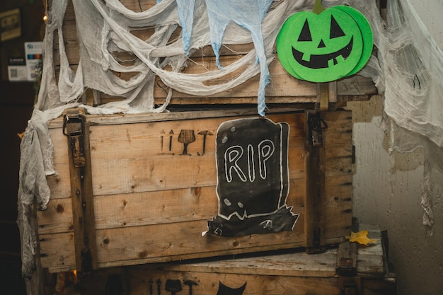 Green halloween pumpkin with painted nose mouth eye on wooden box with gauze as web and tombstone with RIP inscription