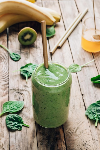 Green healthy smoothie in glass with banana kiwi and spinach on rustic wooden background