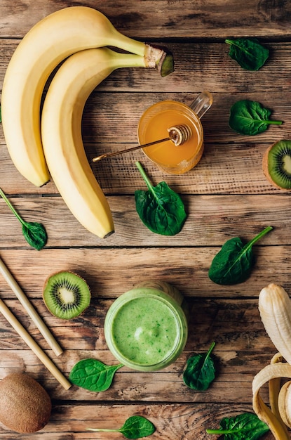 Green healthy smoothie in glass with banana kiwi and spinach on rustic wooden background