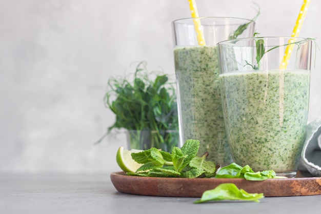 Green healthy smoothie in glasses with ingredients on wooden plate