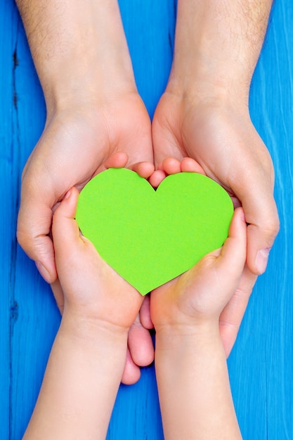 Green heart in hands of adult and child.