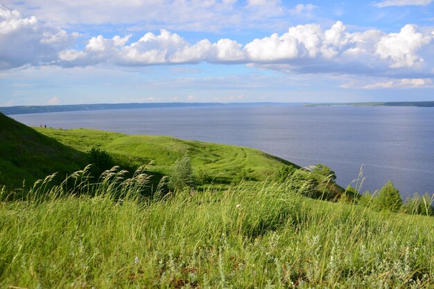 green hills in windy day with blue river and white clouds on horizon