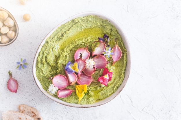 green hummus bowl with baked radish and edible flowers