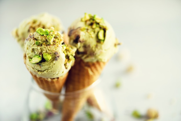 Green ice cream in waffle cone with chocolate and pistachio nuts on grey stone . Summer food concept, copy space. Healthy gluten free ice-cream.