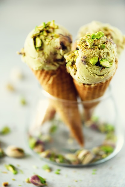 Green ice cream in waffle cone with chocolate and pistachio nuts on grey stone . Summer food concept, copy space. Healthy gluten free ice-cream.