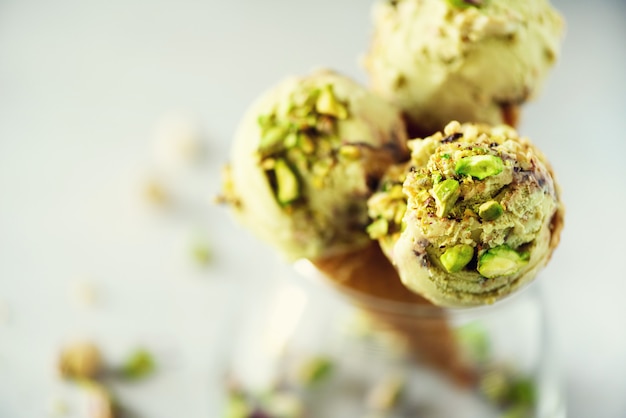 Green ice cream in waffle cone with chocolate and pistachio nuts on grey stone . Summer food concept, copy space. Healthy gluten free ice-cream.