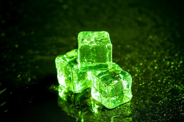 Green ice cubes reflection on black table background.