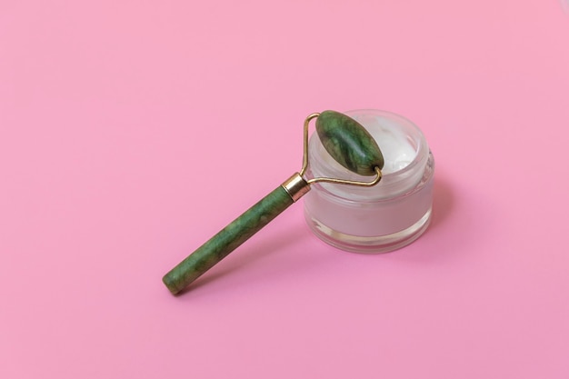 Green jade face roller for anti-age skincare on soft pink background with copy space