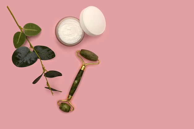 Green jade roller and eucalyptus branch on a pink background